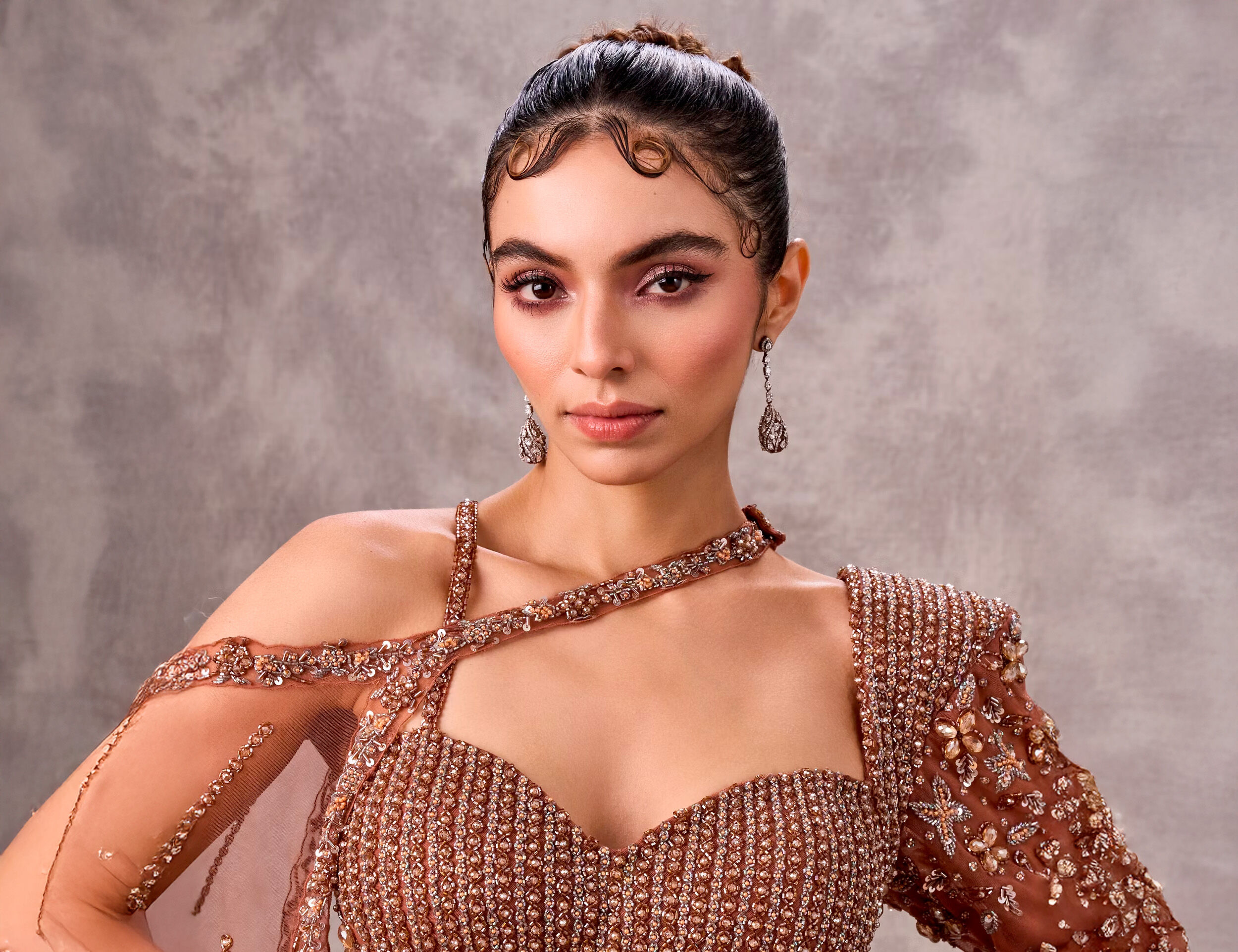 Woman with slicked-back hair and finger waves, wearing a bronze embellished top and dramatic earrings.